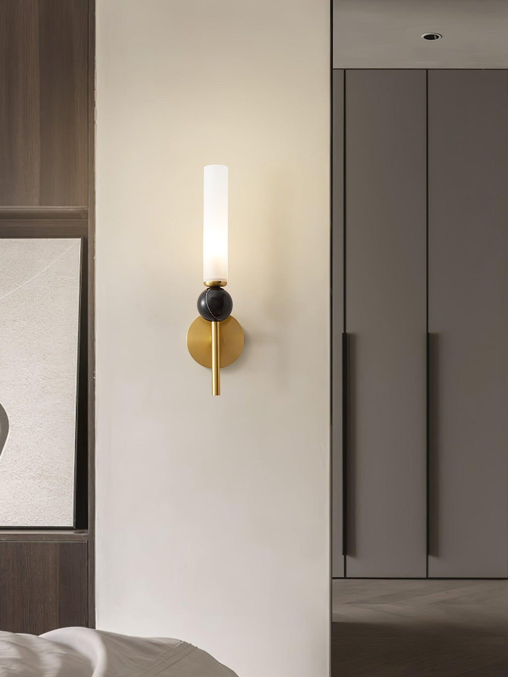 A Clérachic brass wall sconce lit beside a wardrobe door and a framed abstract print in a neutral bedroom corner.