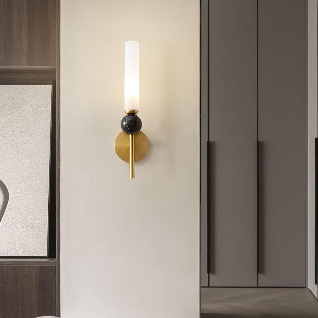 A Clérachic brass wall sconce glows beside dark wood wardrobe doors and a framed abstract print in a bedroom corner.