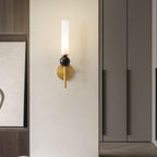 A Clérachic brass wall sconce glows beside dark wood wardrobe doors and a framed abstract print in a bedroom corner.