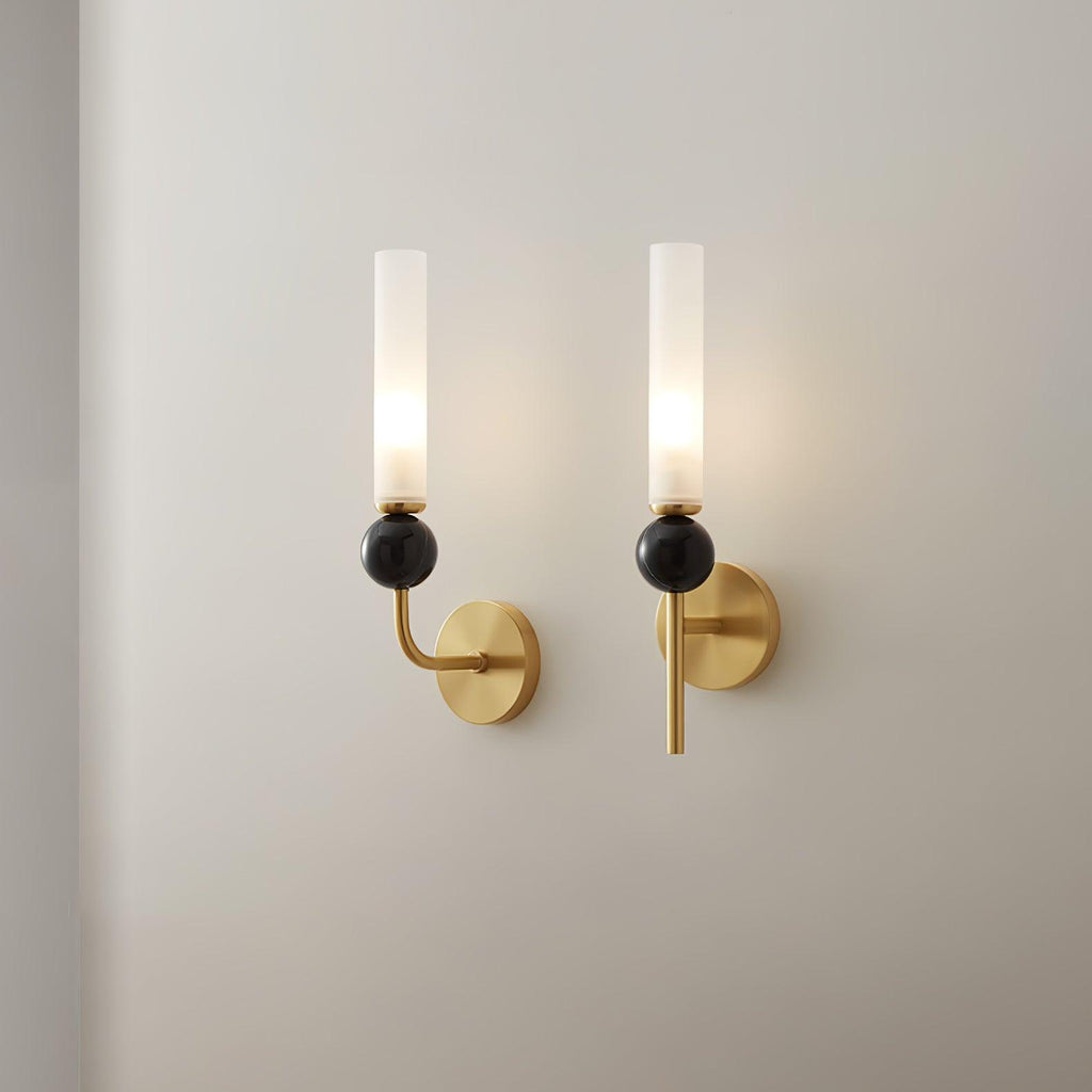 Two Clérachic brass wall sconces mounted side by side on a plain white wall, both lit with black marble orbs, shown for scale.