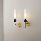 Two Clérachic brass wall sconces mounted side by side on a plain white wall, both lit with black marble orbs, shown for scale.