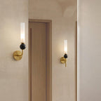 Two Clérachic brass wall sconces flank a wooden door in a warm-toned hallway, each lit with a black marble orb.