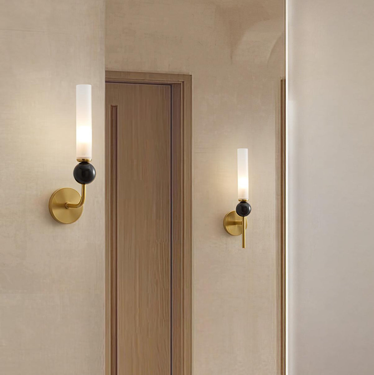 Two Clérachic brass wall sconces flank a wooden door in a warm-toned hallway, each lit with a black marble orb.