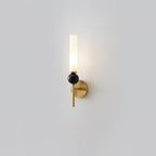 A Clérachic brass-arm wall sconce with a black marble orb, lit and photographed alone against a plain grey background.