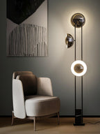 Clérachic floor lamp with its lower ring glowing, standing beside an abstract painting and a beige armchair.