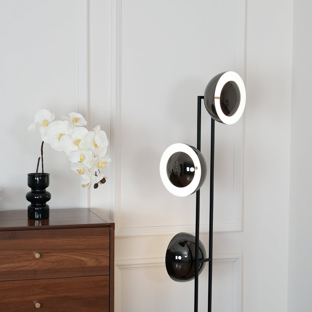 Closer angle of the Clérachic floor lamp's lit top ring beside the same walnut chest of drawers and orchid display.