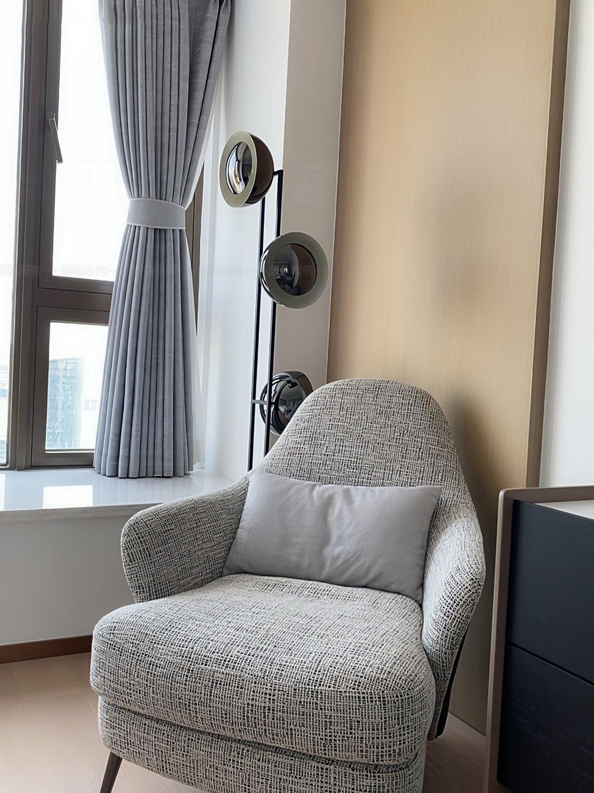 Partial view of the Clérachic floor lamp beside a curtained window and a grey tweed armchair in a quiet corner.