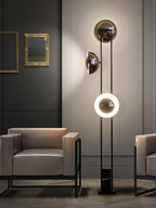 Clérachic floor lamp with its lower ring lit, framed between a gilt mirror and two matching grey armchairs.