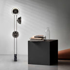 Clérachic three-light floor lamp beside a black cube side table holding a glass vase and stacked magazines.