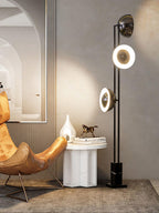 Clérachic floor lamp with its middle ring lit, standing near a gilt mirror, an armchair and a marble side table.
