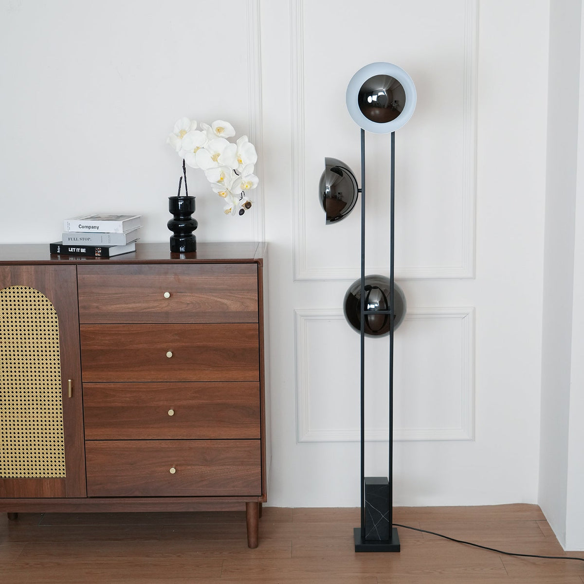 Top ring of the Clérachic floor lamp glowing pale white beside a rattan-panelled chest of drawers and an orchid.