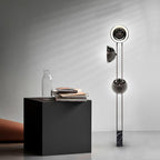 Clérachic floor lamp lit at the top, standing beside a black cube side table holding a vase and stacked magazines.