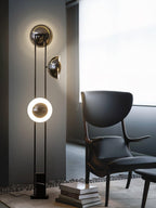 Clérachic floor lamp with all three heads lit, standing beside a dark leather chair and a stack of books.