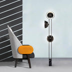 Clérachic floor lamp with its top dome lit gold, standing beside a grey chair with an orange accent stool.