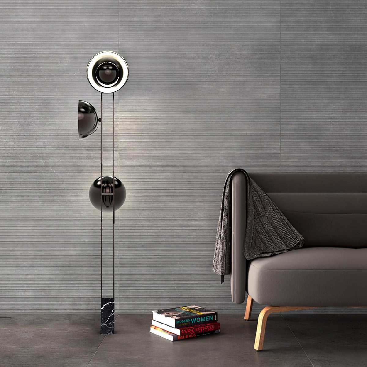 Clérachic three-light floor lamp glowing against a grey wall beside a sofa with a folded throw and a stack of books.