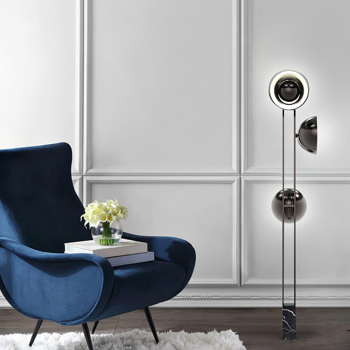 Clérachic floor lamp with its top ring lit, standing beside a blue velvet armchair topped with a vase of flowers.