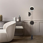 Full-height view of the Clérachic floor lamp, top ring lit warm white, beside a round table with ceramics in a bright room.