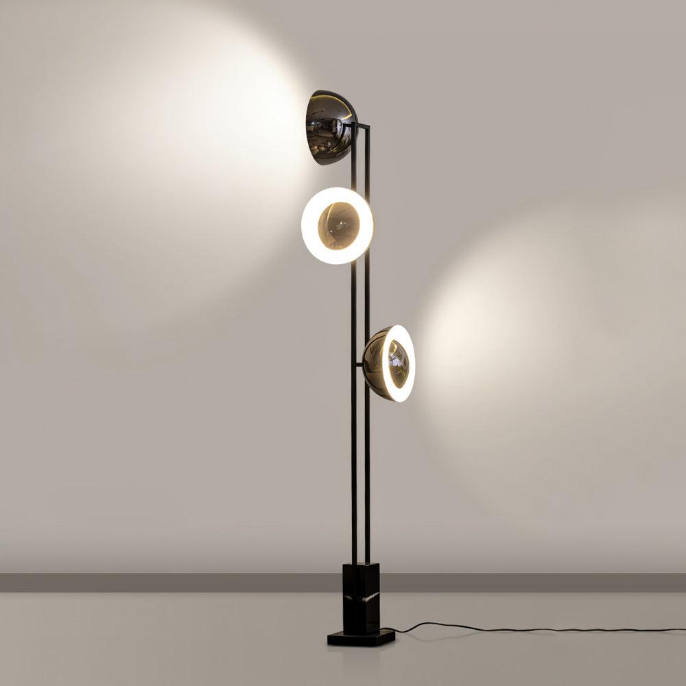 Middle and lower rings of the Clérachic floor lamp lit warm white, reflected faintly on a plain studio floor.