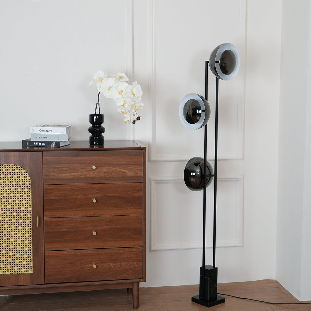 Three lit heads of the Clérachic floor lamp shown close beside a walnut chest of drawers with an orchid on top.