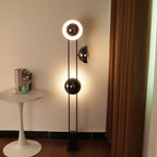 Clérachic floor lamp with its top ring lit, positioned near a round white table and curtain in a warm-toned room.