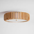 Overhead studio view of this Clérachic ceiling light, lit, wood slats spread in a wide oval.