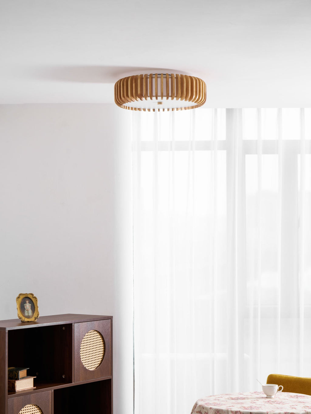 Seen small in a room corner, this Clérachic ceiling light hangs near sheer curtains and a dark cabinet.