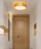 Lit in a hallway above a wood-panelled door, this Clérachic ceiling light casts a warm glow.