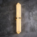 The brass-band sconce lit on grey concrete, seen full length from top point to bottom point.