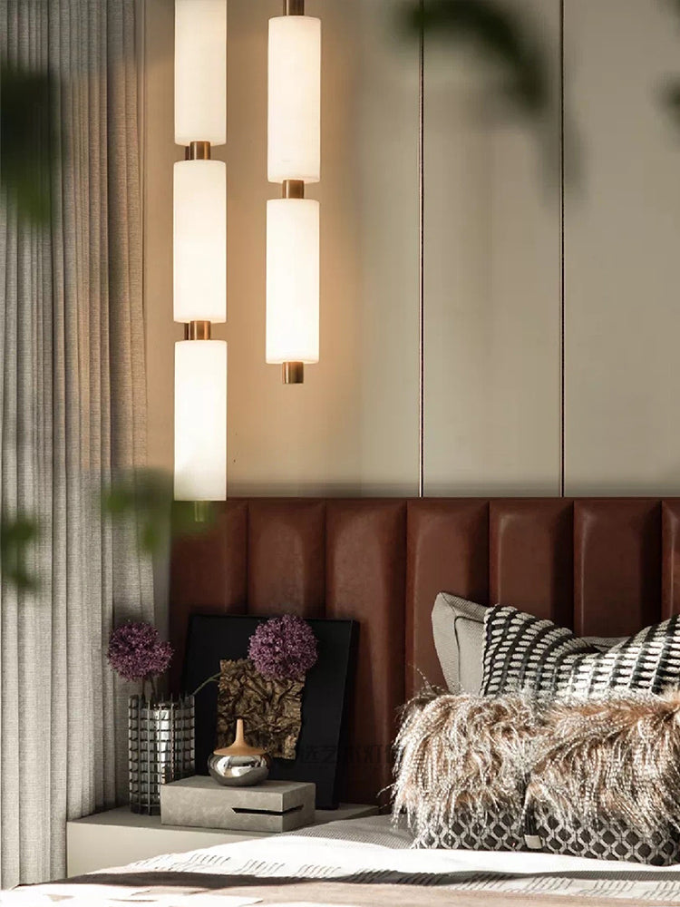 Close bedroom crop of the lit Zovarion pendants glowing against a panelled wall, framed by green leaves.