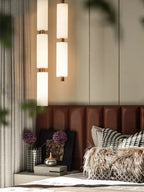 Close bedroom crop of the lit Zovarion pendants glowing against a panelled wall, framed by green leaves.