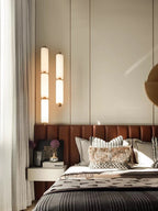 Two Zovarion alabaster pendants lit at staggered drops beside a tan leather headboard in a bedroom.
