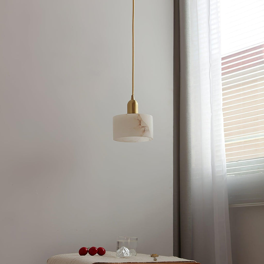 The Brio pendant unlit in daylight, its long brass cord dropping from the ceiling beside a sheer-curtained window.
