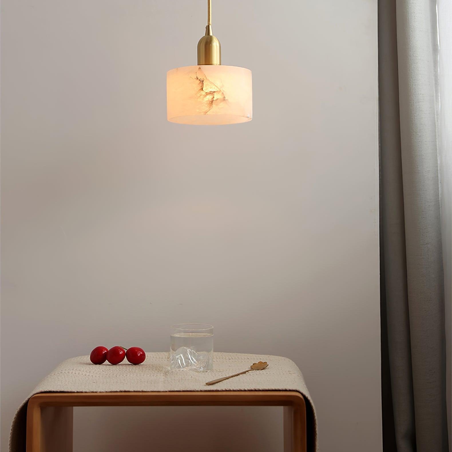 Brio pendant lit above a wooden side table, the alabaster shade casting a warm glow across the pale wall.