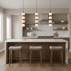 Three four-ball Orbique pendants lit in a row above a white marble kitchen island with wood stools