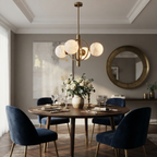 A brushed-brass Clérachic chandelier lights a round dining table with navy velvet chairs and a brass mirror.