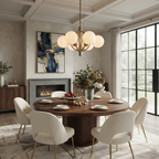 The brushed-brass Clérachic chandelier glows above a round table beneath a coffered ceiling and fireplace.