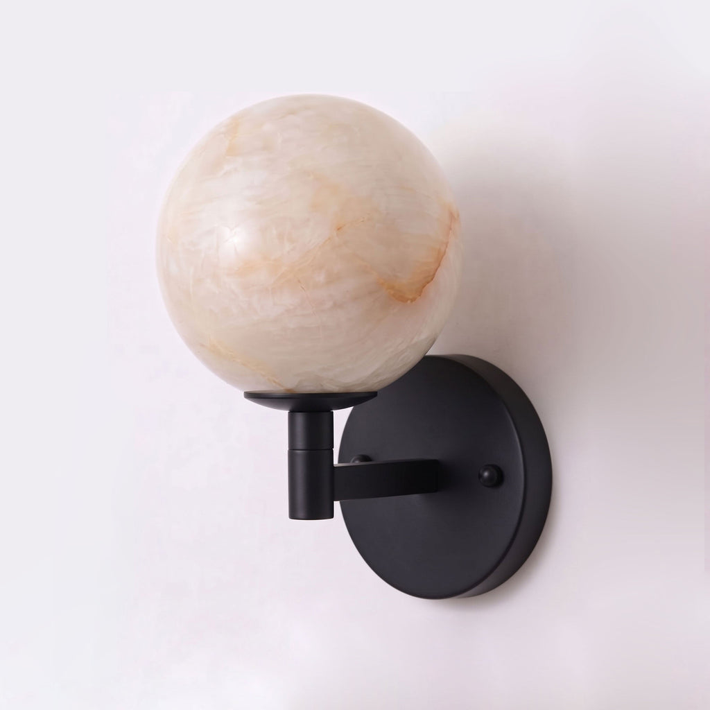 Set against a plain backdrop, the matte black finish of this Clérachic sconce holds a single alabaster globe shade.