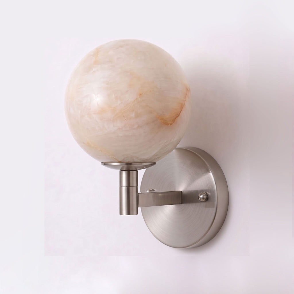 Photographed unlit on white, the nickel finish of this Clérachic sconce curves up to a round alabaster globe.
