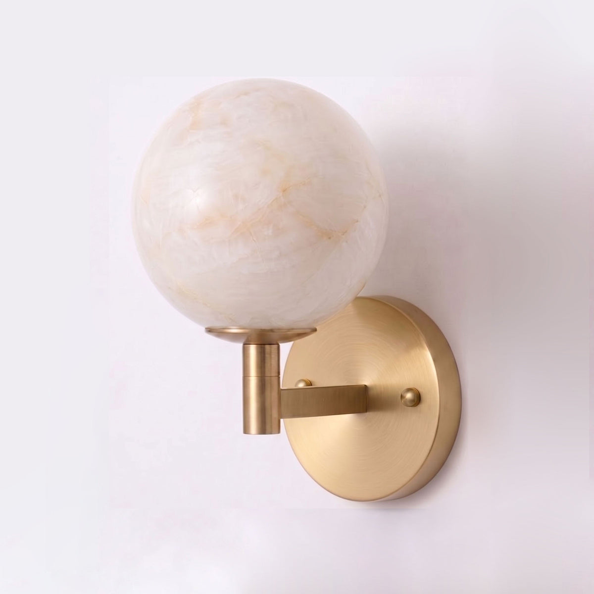 Photographed from another angle on a plain backdrop, this Clérachic sconce's brass finish highlights the veining in its alabaster globe.