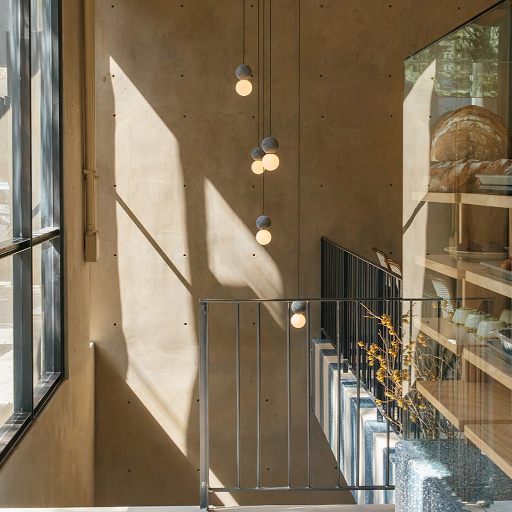 Several dark stone pendant lights from this Clérachic collection hang above a staircase in a sunlit, wood-panelled stairwell.
