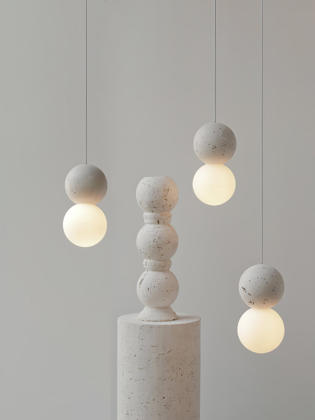 Grey stone-textured pendants from this Clérachic collection hang beside a stacked stone pedestal on a plain backdrop.