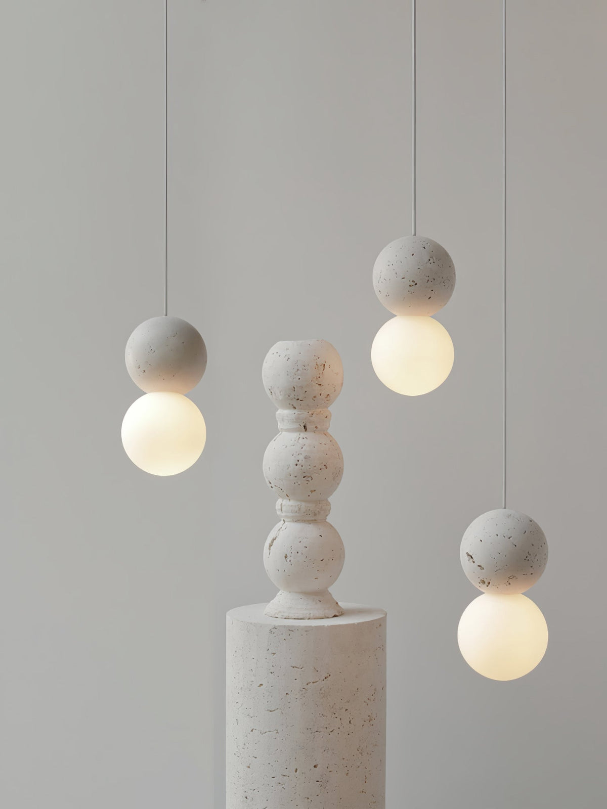 Grey stone-textured pendants from this Clérachic collection hang beside a stacked stone pedestal on a plain backdrop.