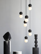 Several dark sphere pendants from this Clérachic collection hang above dark stone and ceramic pedestals on a plain grey backdrop.