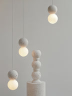 This Clérachic pendant, a single grey stone-textured sphere, hangs beside a taller stacked stone pedestal.