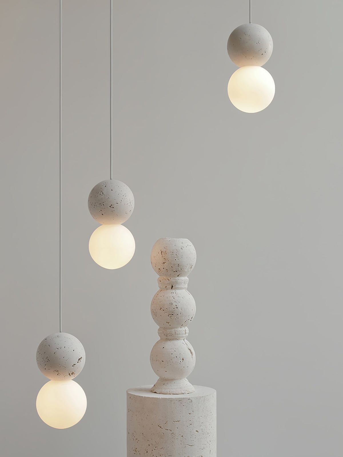 This Clérachic pendant, a single grey stone-textured sphere, hangs beside a taller stacked stone pedestal.