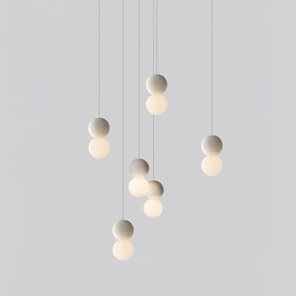 A cluster of pale sphere pendants from this Clérachic collection hangs at staggered heights against a plain light-grey backdrop.