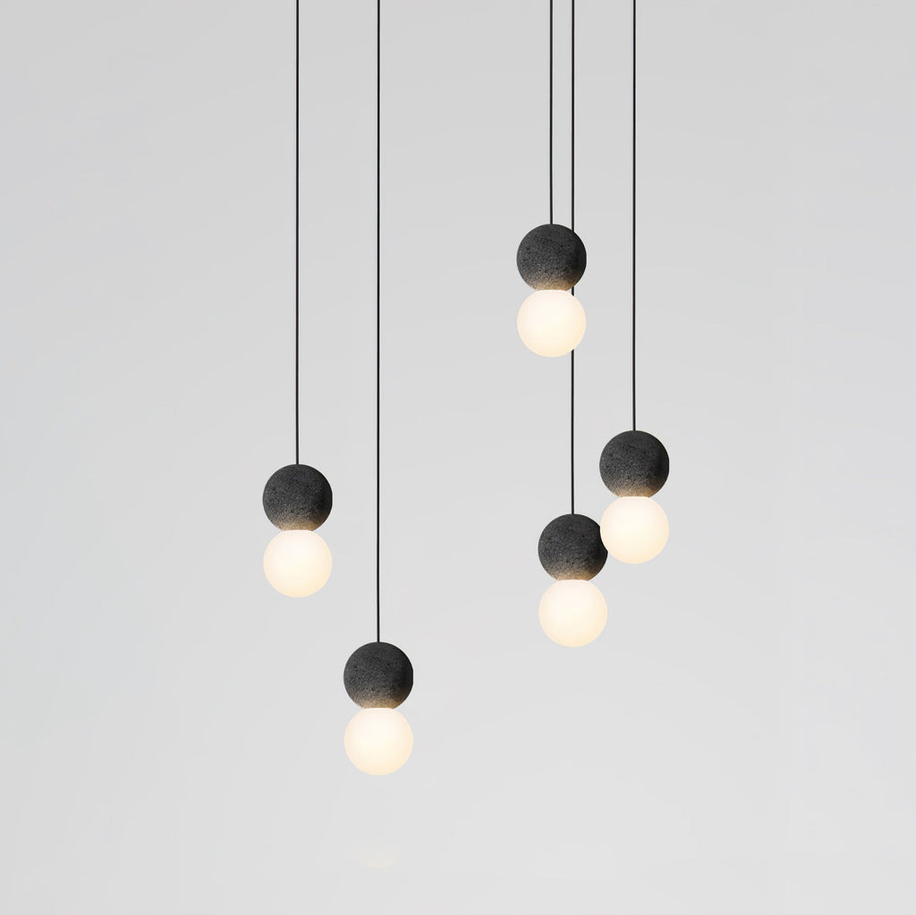 This Clérachic pendant cluster hangs in two staggered rows, dark spheres and lit glass globes set against a plain grey wall.