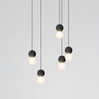 This Clérachic pendant cluster hangs in two staggered rows, dark spheres and lit glass globes set against a plain grey wall.