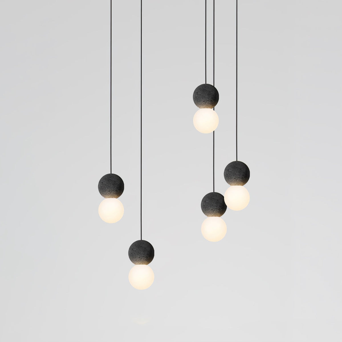 This Clérachic pendant cluster hangs in two staggered rows, dark spheres and lit glass globes set against a plain grey wall.