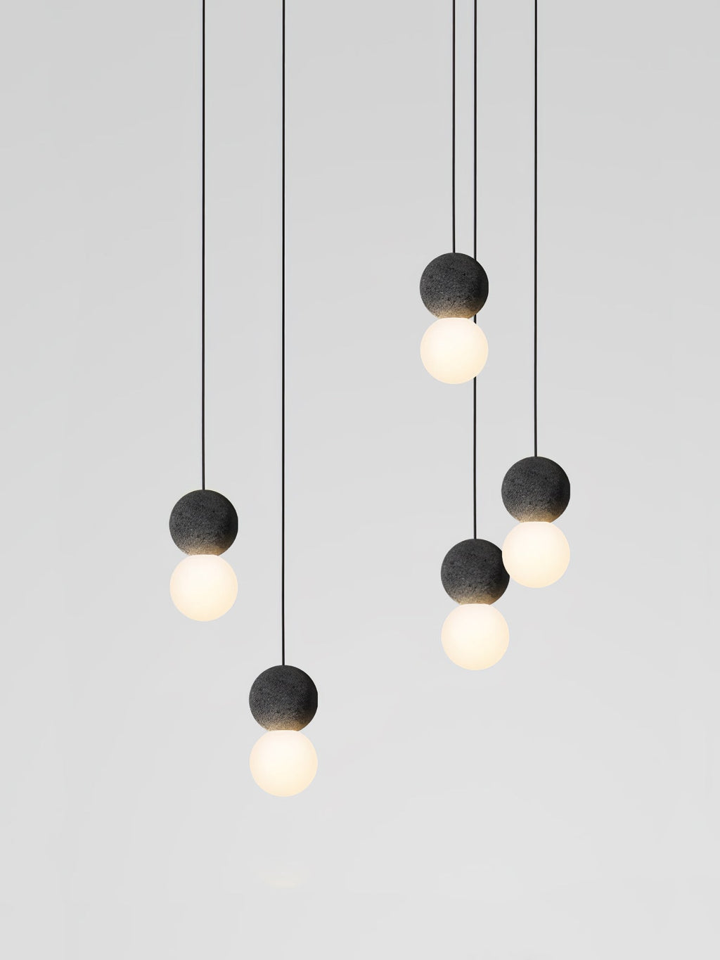 This Clérachic pendant cluster drops at seven different lengths, its dark spheres and glass globes glowing softly against grey.